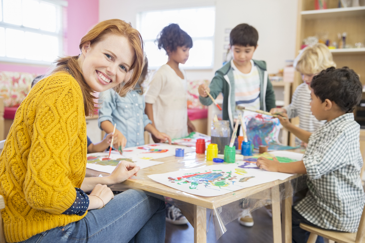 Erzieherin bastelt mit Kindern und malt mit ihnen Bilder
