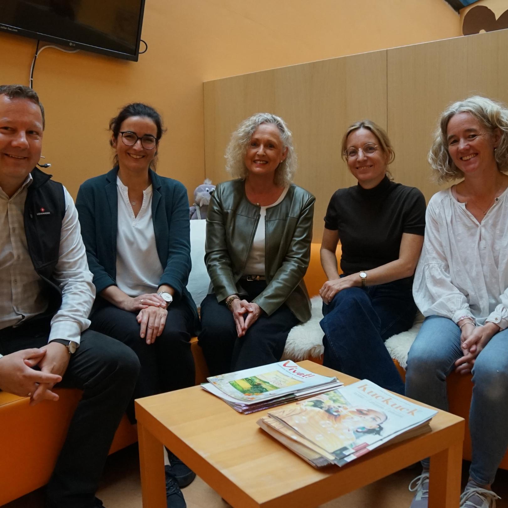 4 Frauen und 1 Mann sitzen auf einem orangenen Sofa