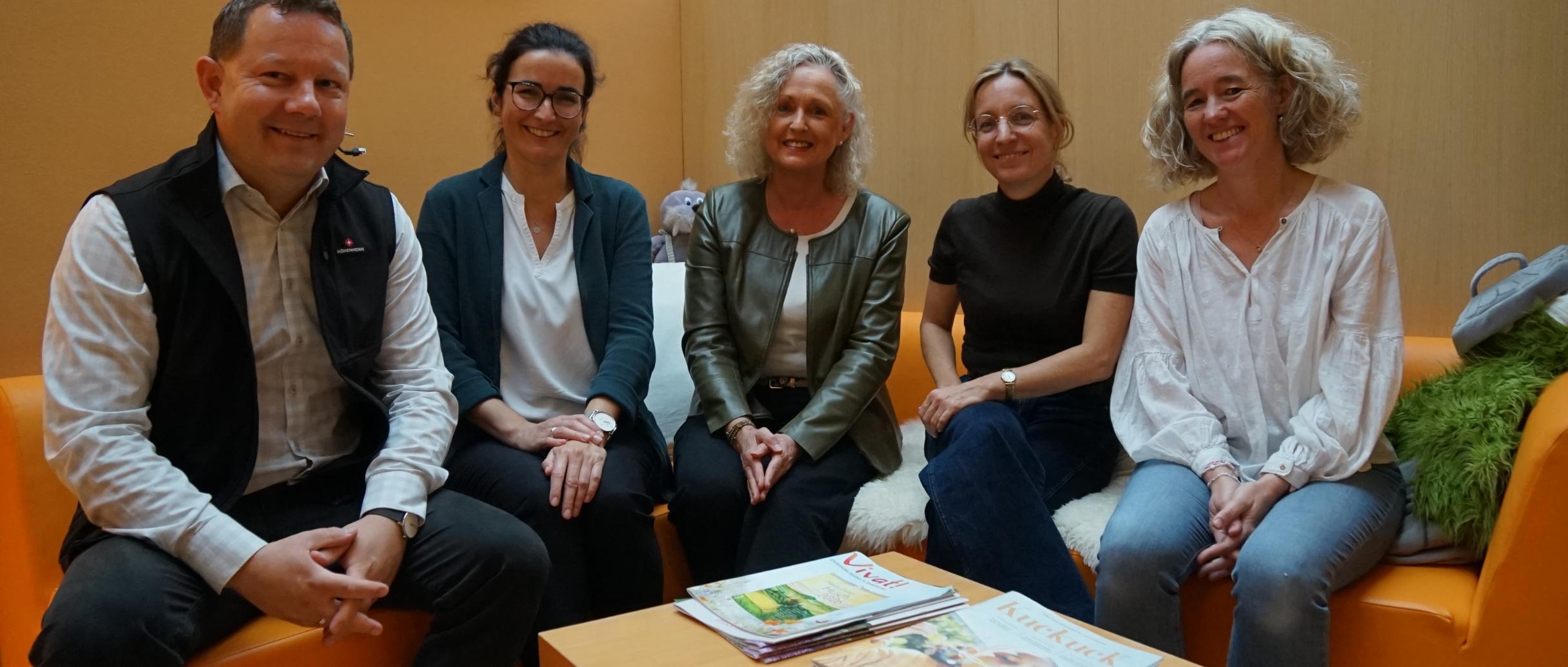 4 Frauen und 1 Mann sitzen auf einem orangenen Sofa