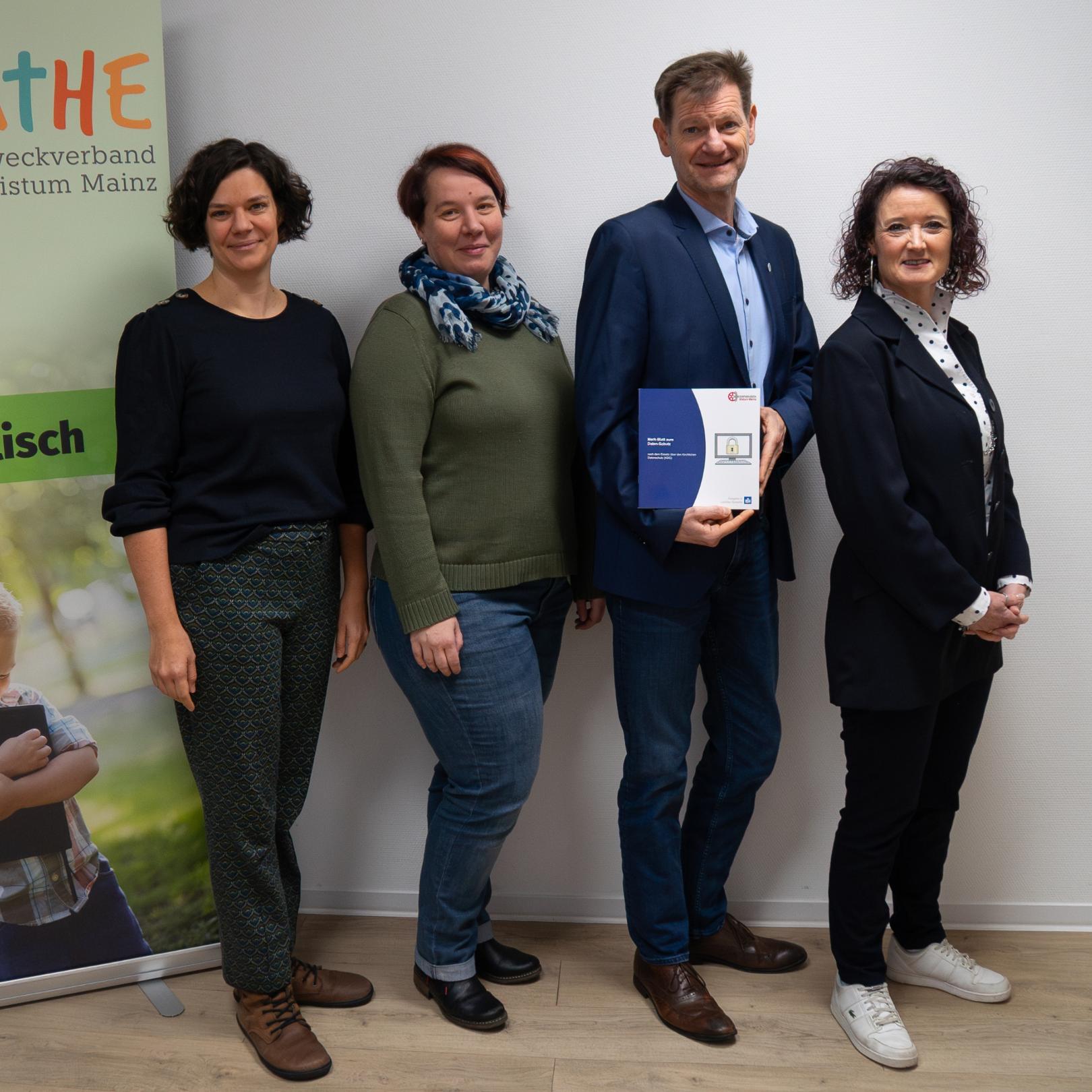 4 Menschen (3 Frauen und 1 Mann) posieren mit Datenschutzbroschüre vor Unikathe Banner