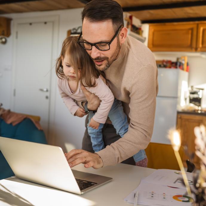Vater mit Kind auf dem Arm arbeitet am Computer im Stehen