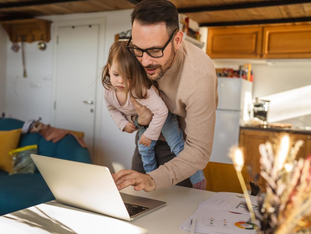 Vater mit Kind auf dem Arm arbeitet am Computer im Stehen