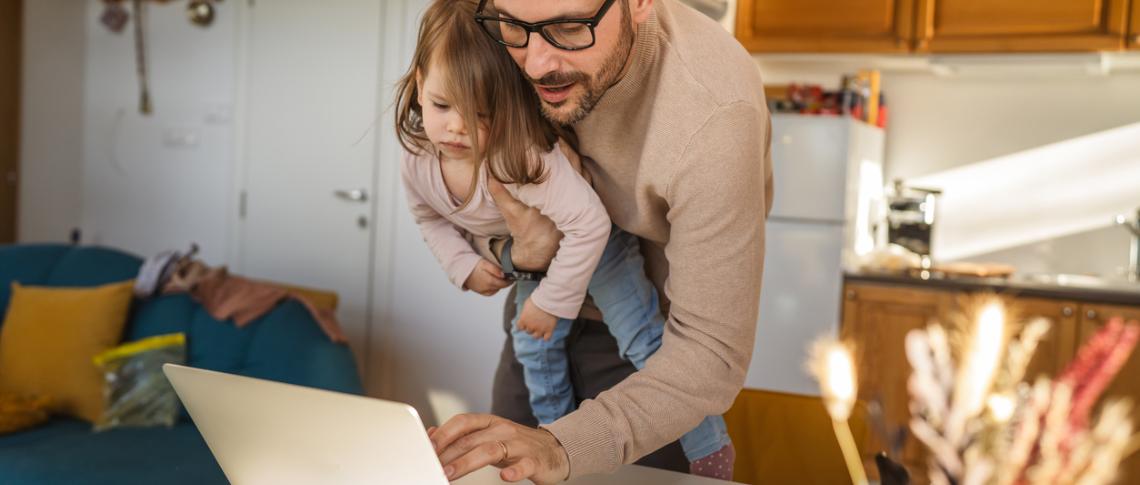 Vater mit Kind auf dem Arm arbeitet am Computer im Stehen