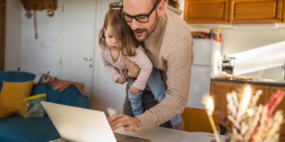 Vater mit Kind auf dem Arm arbeitet am Computer im Stehen