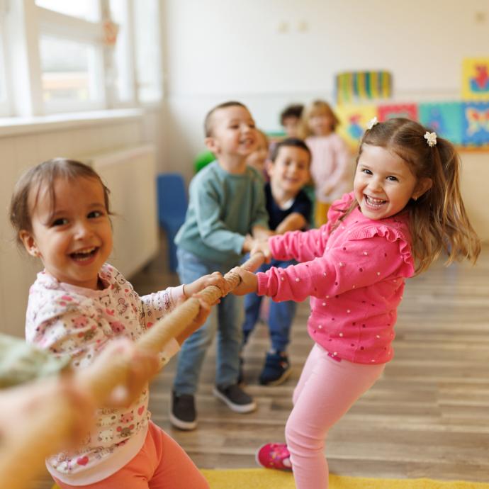Viele lachende Kinder ziehen gemeinsam an einer Stange
