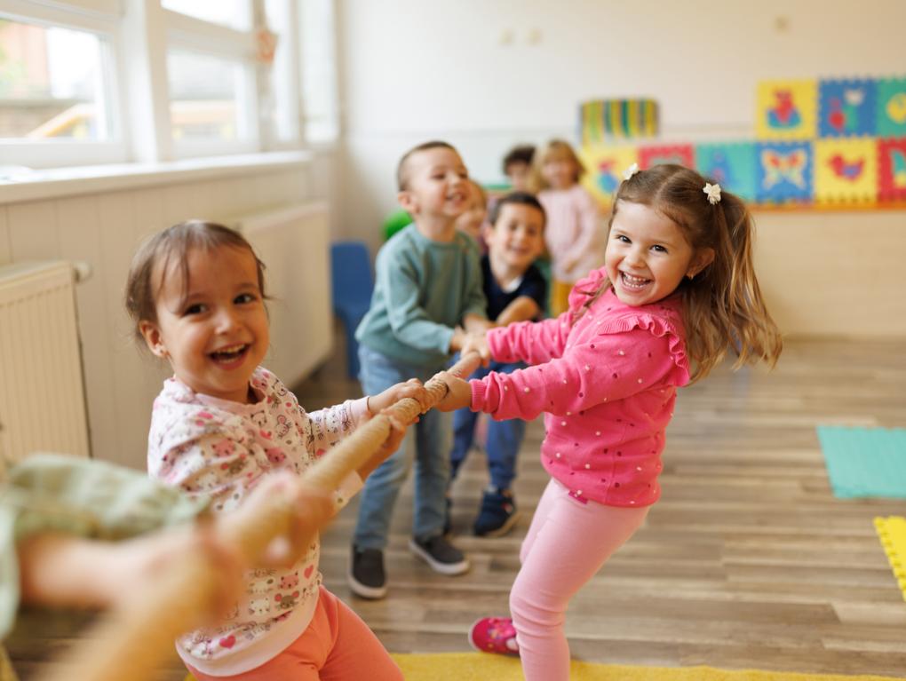 Viele lachende Kinder ziehen gemeinsam an einer Stange