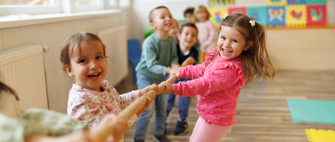 Viele lachende Kinder ziehen gemeinsam an einer Stange
