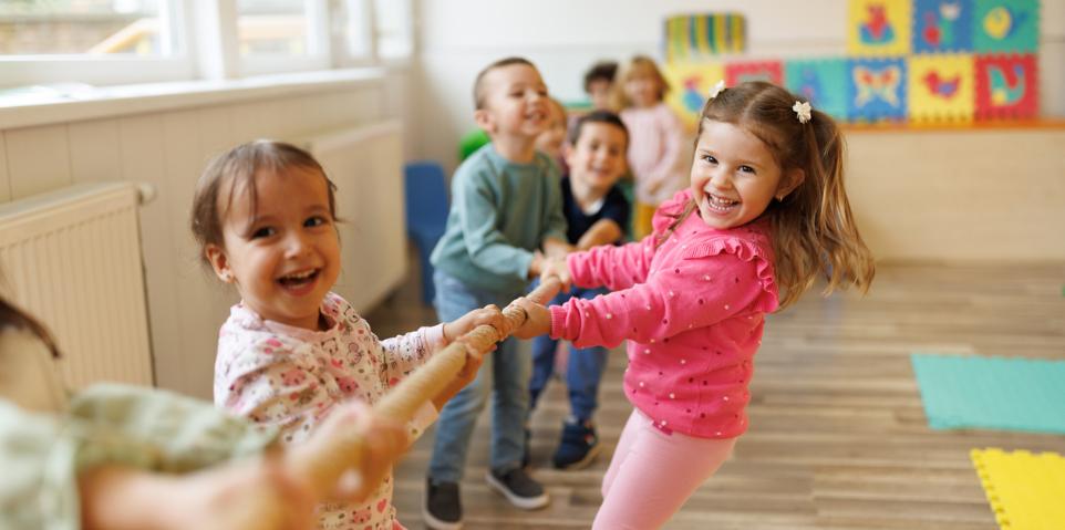 Viele lachende Kinder ziehen gemeinsam an einer Stange