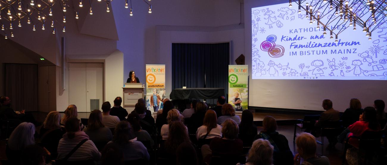 Großer Saal mit vielen sitzenden Menschen die einer Frau am Rednerpult zuhören