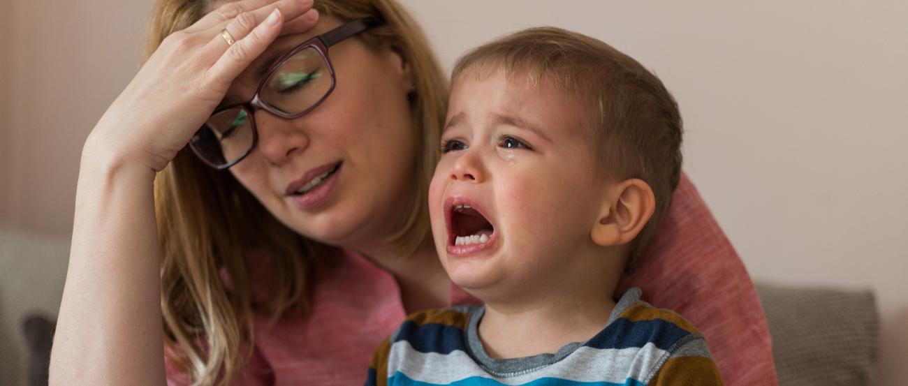 Erschöpfte Mutter mit schreiendem Kind auf dem Schoß