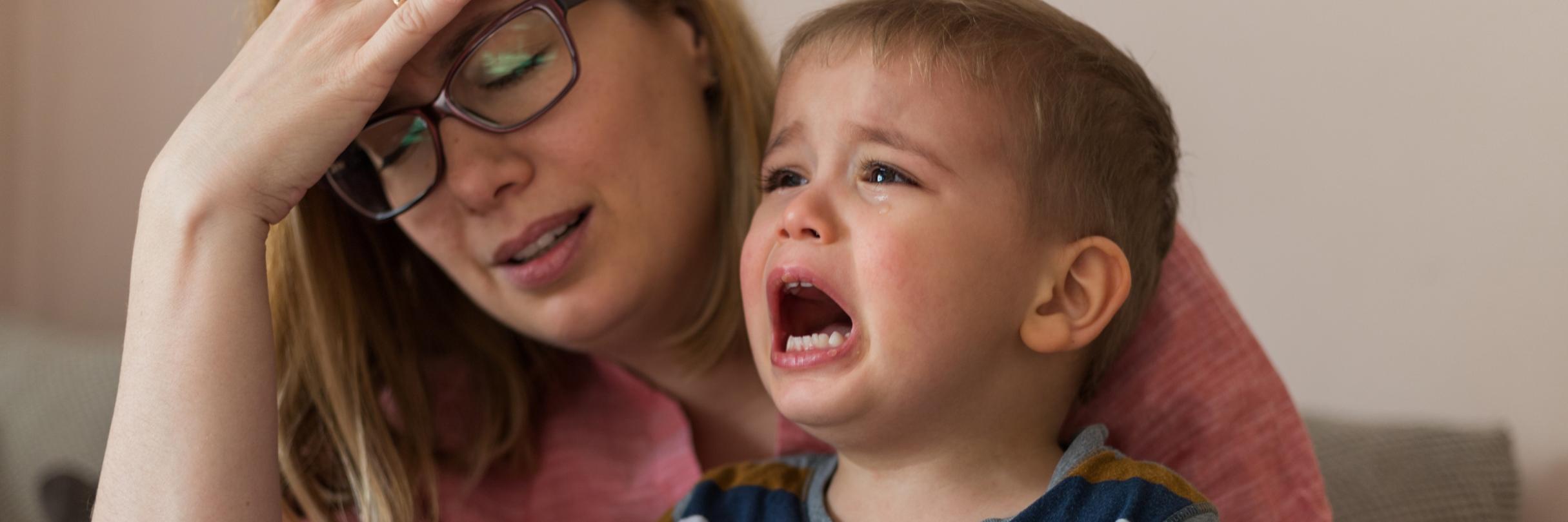 Erschöpfte Mutter mit schreiendem Kind auf dem Schoß