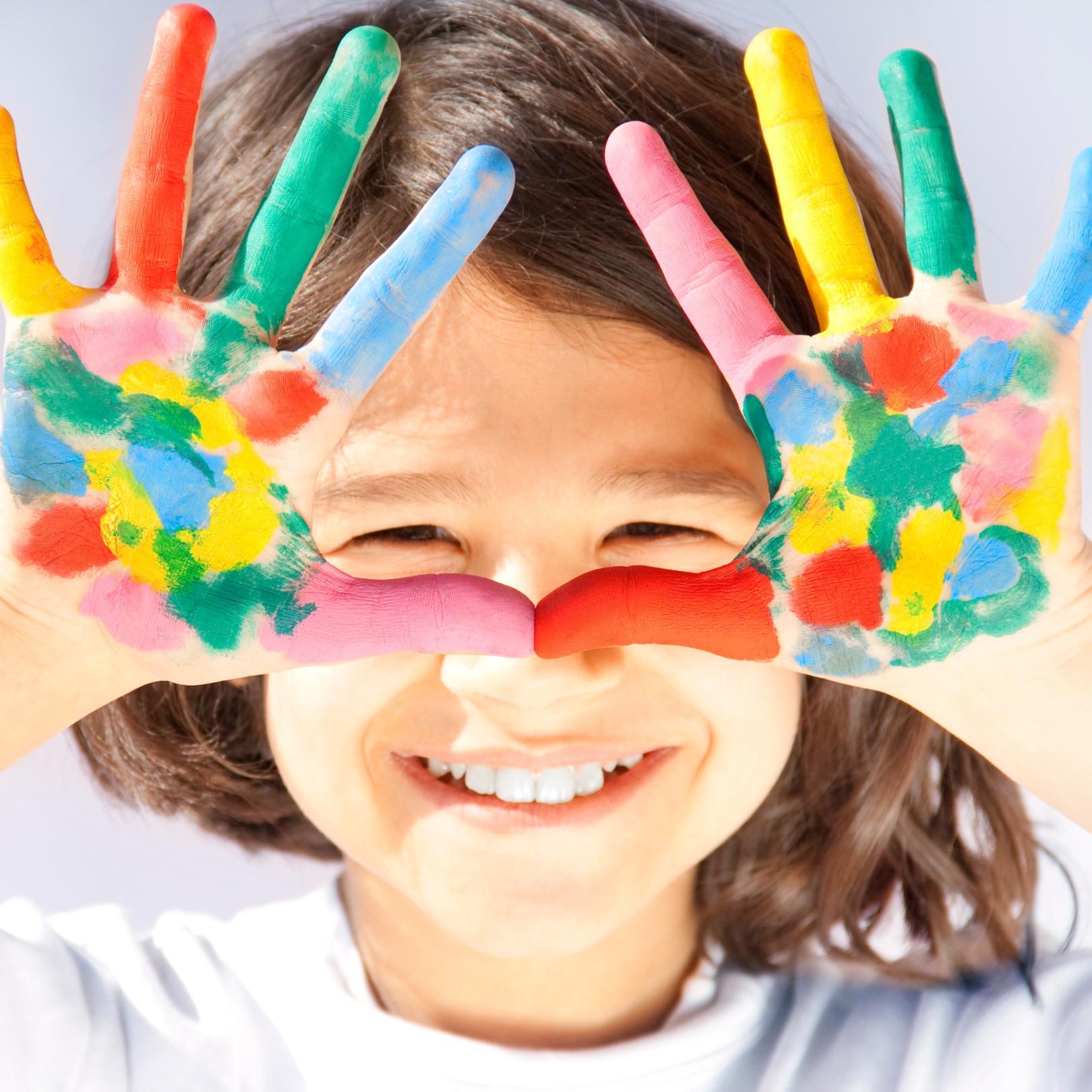 Ein Kind hält beide Hände vor das Gesicht. Die Handflächen sind mit bunten Farben bemalt. Durch die Öffnung in der Mitte sind die Augen des Kindes zu sehen.