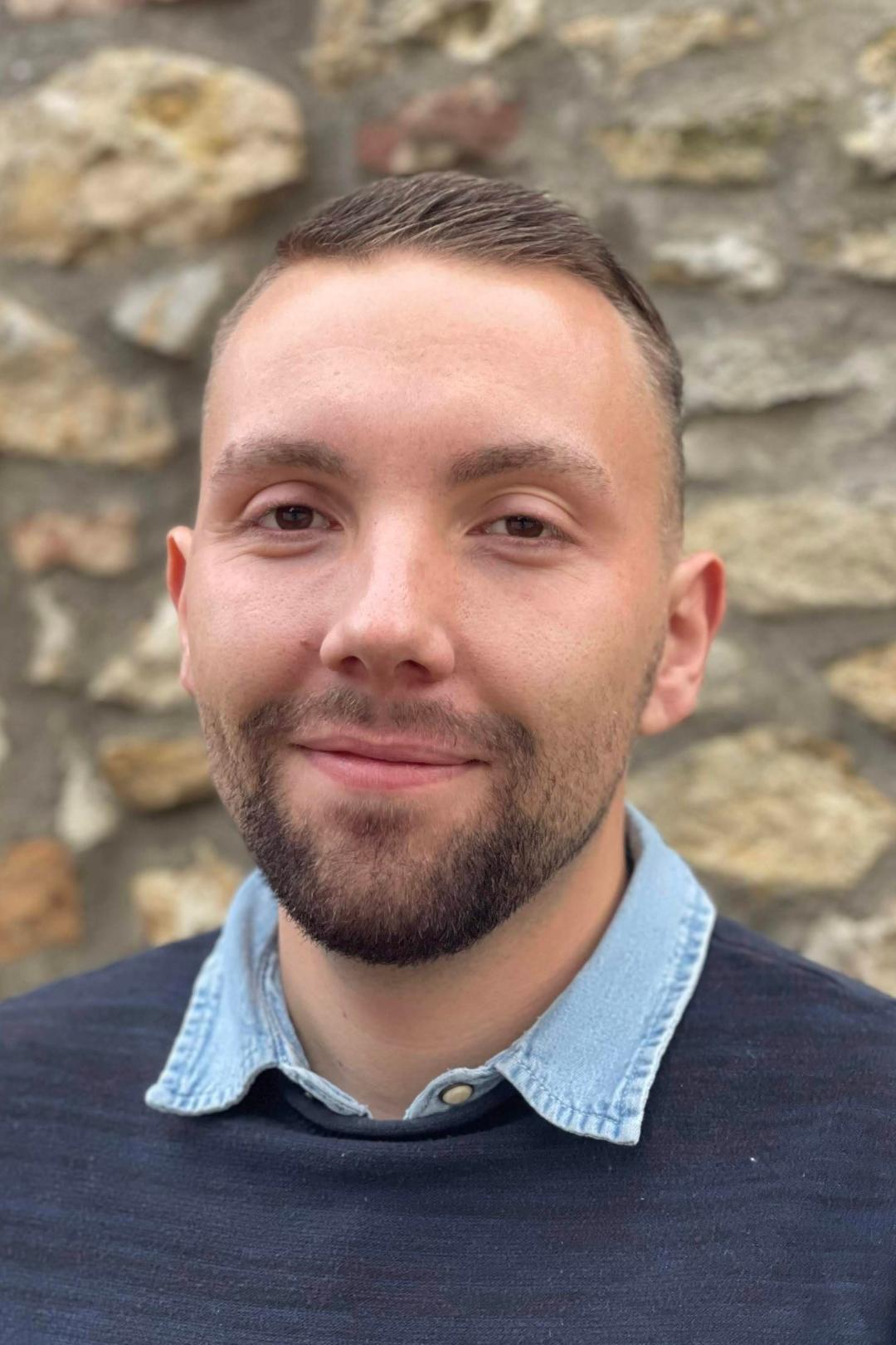 Ein Mann, Ende 20 mit kurzen, braunen Haaren und 3-Tage-Bart