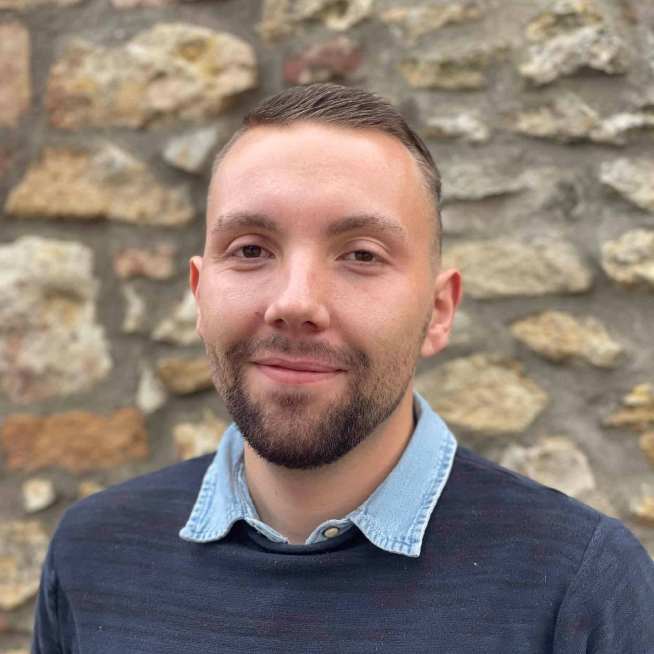 Ein Mann, Ende 20 mit kurzen, braunen Haaren und 3-Tage-Bart